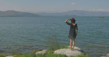 Kız rıhtımda takılıyor, sahilde yürüyor. Kameranın önünde poz vermek, gülümsemek, kumda yalın ayak yürümek, rüzgarın şalla oynaması.