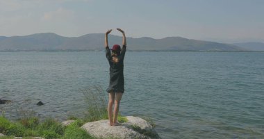 Kız rıhtımda takılıyor, sahilde yürüyor. Kameranın önünde poz vermek, gülümsemek, kumda yalın ayak yürümek, rüzgarın şalla oynaması.