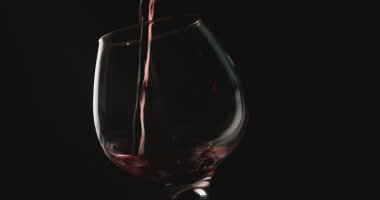 Kırmızı şarabı bir bardağa dolduruyorum, siyah arkaplanın önünde.