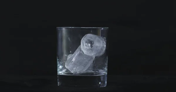 Ice cubes melt in the alcohol, whiskey glass and smoke is floating against a black background