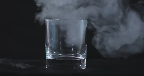 黒い背景と浮遊煙を背景にした空のウイスキー アルコールガラス — ストック写真