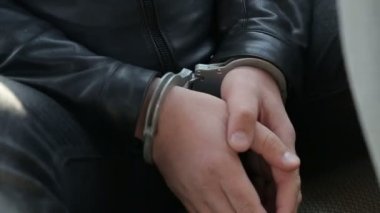 Tutuklu bir kişi, üniformalı insanlar eşliğinde kelepçelenmiş..