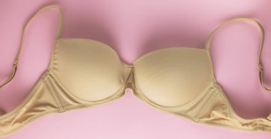 Kadın meme hastalığı sembolü olarak pembe arka plan bej sutyen. Göğüs kanseri duyarlılığı ayı. Minimalist tarzı. Üstten görünüm. Düz yatıyordu.