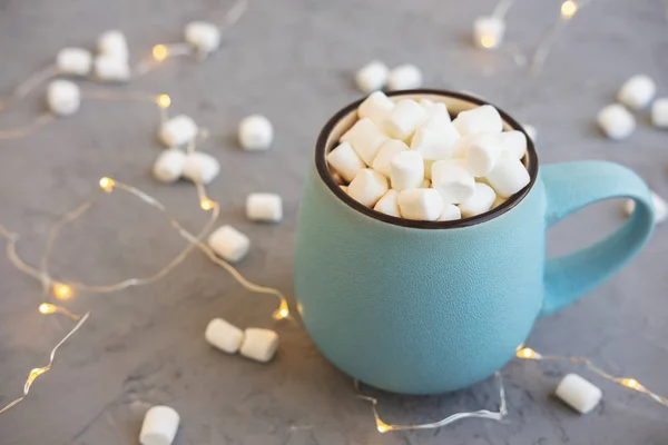 Taza azul de café sobre fondo de hormigón gris con malvavisco y guirnalda. Acogedora bebida concepto otoño e invierno . — Foto de Stock