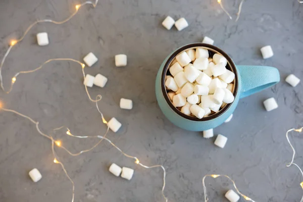 Blå kopp kaffe på grå betong bakgrund med marshmallow och garland. Mysiga drink hösten och vintern koncept. Ovanifrån. Lekmanna-platt. — Stockfoto