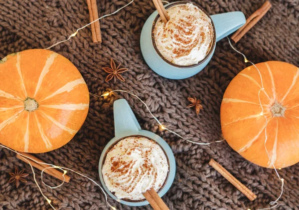 Mug of coffee, cocoa or hot chocolate with whipped cream and cinnamon on scarf with pumpkin, leaves, garland, anise star. Pumpkin latte - cozy drink for cold autumn or winter. Flat lay. Top view. — Stock Photo, Image