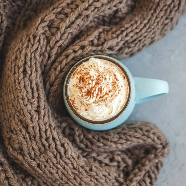 Kubek kawy, kakao lub gorąca czekolada z bitą śmietaną i cynamonem na betonowe podłoże i szalik. Dyni latte jesień przytulny drink na zimne wieczory. Pojęcie ciepła domu jesienią lub zimą. — Zdjęcie stockowe