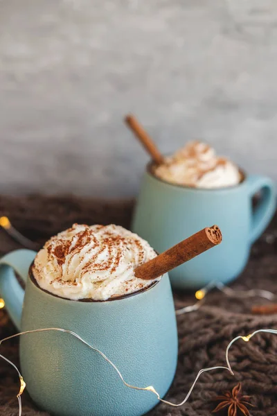 Mug of coffee, cocoa or hot chocolate with whipped cream and cinnamon on scarf with leaves, garland, anise star. Pumpkin latte - cozy drink for cold autumn or winter. — Stock Photo, Image