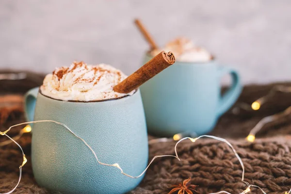 Mug of coffee, cocoa or hot chocolate with whipped cream and cinnamon on scarf with leaves, garland, anise star. Pumpkin latte - cozy drink for cold autumn or winter. — Stock Photo, Image