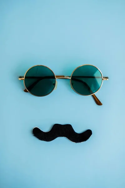 Runde grüne Brille und schwarzer Schnurrbart auf blauem Hintergrund. Das Konzept des Mannes Vatertag, Monat des Prostatakrebses. flach lag. Ansicht von oben. — Stockfoto