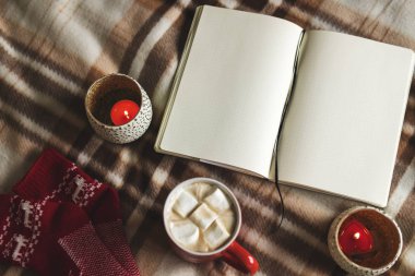 Sonbahar ve kış defter, kalem, mumlar, örme kırmızı çorap, kupa kakao, kahve veya sıcak çikolata hatmi ekose üzerinde arka plan. Sıcak rahat ev planları çizim çalışmalarının kavramı.