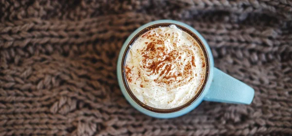 Mug of coffee, cocoa or hot chocolate with whipped cream and cinnamon on knitted scarf. Pumpkin latte autumn cozy drink for cold evenings. Concept of warm home autumn or winter. — Stock Photo, Image