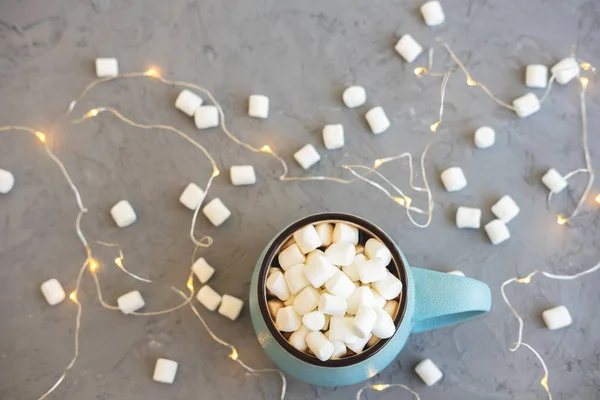 Blue cup of coffee on gray concrete background with marshmallow and garland. Cozy drink autumn and winter concept. Top view. Flat lay. — Stock Photo, Image