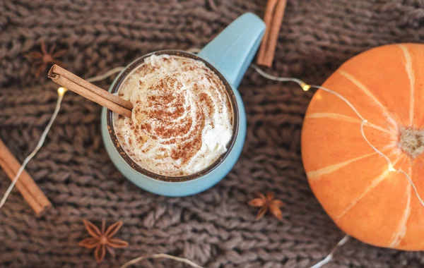 Mug of coffee, cocoa or hot chocolate with whipped cream and cinnamon on scarf with pumpkin, leaves, garland, anise star. Pumpkin latte - cozy drink for cold autumn or winter. Flat lay. Top view. — Stock Photo, Image
