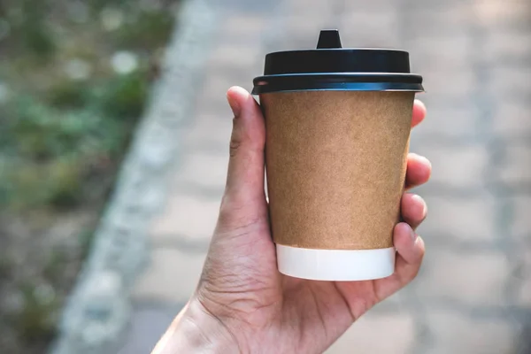 Coffee paper crafting cup holds female hand on a blurred background. Place for text or logo.