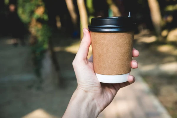 Coffee paper crafting cup holds female hand on a blurred background. Place for text or logo.