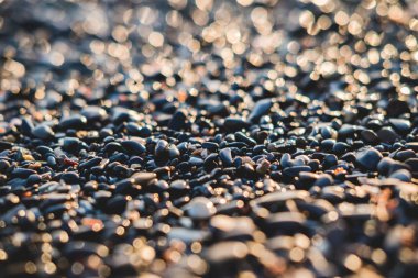 Deniz kenarında Bokeh etkisi olan küçük taşlar. Bulanık dekoratif arka plan, metin için yer. Yaz duvar kağıdı, güneşli gün batımı ışığı.