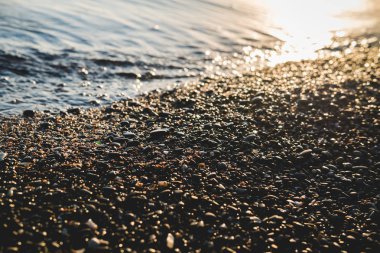 Bokeh etkisi ile deniz tarafından küçük taşlar. Bulanık dekoratif tatil ve tatil arka plan, metin için yer. Yaz duvar kağıdı, güneşli gün batımı ışık.