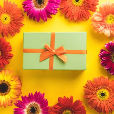 Güneşli sarı arka plan üzerinde parlak güzel gerbera çiçek ile Hediye kutusu. Yeni Yıl, Noel, Doğum Günü, Yıldönümü kavramı. Üst te. Yassı lay.