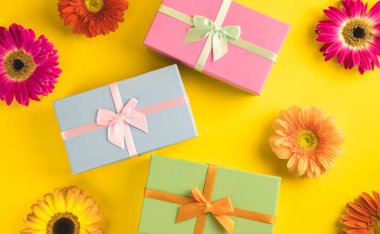 Güneşli sarı arka plan üzerinde parlak güzel gerbera çiçek ile Hediye kutusu. Yeni Yıl, Noel, Doğum Günü, Yıldönümü kavramı. Üst te. Yassı lay.