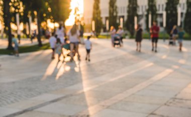 Parktaki ağaçlardan gelen uzun gölgelerle bulanık arka plan. Parkta yürüyen tanınmayan insanların siluetleri.