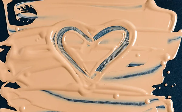 Texture of liquid foundation on dark surface with figure in the shape of heart. Cosmetics advertising concept.