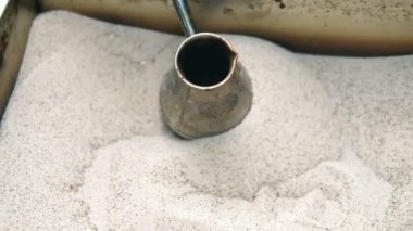 Mans el Türk tutar ve kum içinde Türk kahvesi hazırlar. Yavaş çekim.