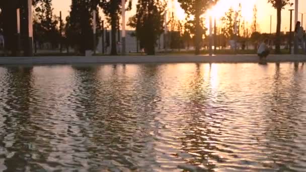 Puesta de sol en el lago en verano u otoño parque de la ciudad. En segundo plano álamos y personas irreconocibles caminan . — Vídeo de stock