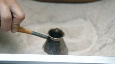 Mans el Türk tutar ve kum içinde Türk kahvesi hazırlar. Yavaş çekim.
