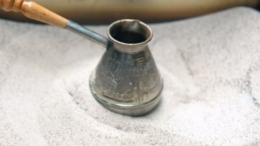 Mans el Türk tutar ve kum içinde Türk kahvesi hazırlar. Yavaş çekim.