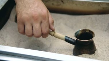 Mans el Türk tutar ve kum içinde Türk kahvesi hazırlar. Yavaş çekim.