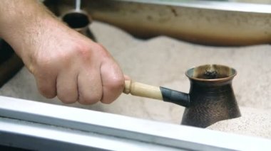 Mans el Türk tutar ve kum içinde Türk kahvesi hazırlar. Yavaş çekim.