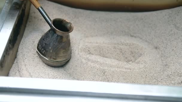 Mans hand holds Turk and prepares Turkish coffee in the sand in it. Slow motion. — Stock Video