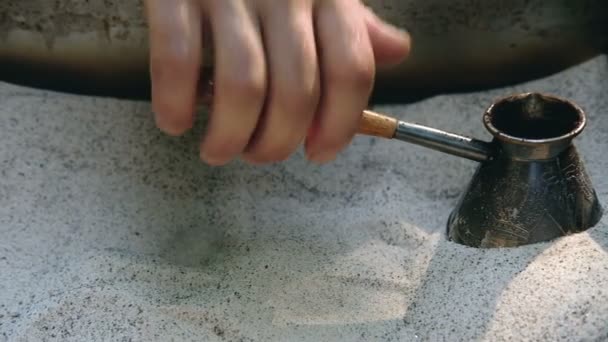 Mans hand holds Turk and prepares Turkish coffee in the sand in it. Slow motion. — Stock Video