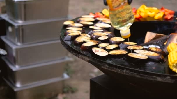 Churrasqueira redonda com lareira no interior. Refeições para piquenique de verão estão sendo preparadas: milho, berinjela, pimentão, kebab. Mãos masculinas em luvas pretas virar comida com pinças de churrasco . — Vídeo de Stock