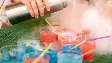 Kadın barmen el termos sigara kokteyl döker. Tüpleri yeşil arka plan üzerinde durmak ile çok renkli bardak.