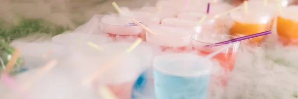 Steaming multi-colored cocktails with dry ice standing on green background. — Stock Photo, Image