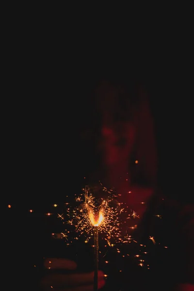 Girl in neon light on dark background, dressed in green glasses, holds a burning sparkler front of her. — Stock Photo, Image