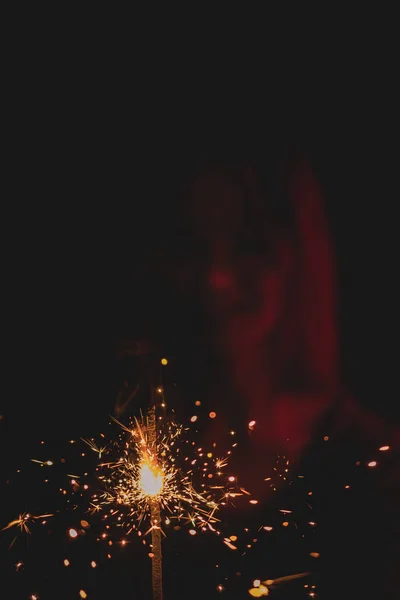 Girl in neon light on dark background, dressed in green glasses, holds a burning sparkler front of her. — Stock Photo, Image