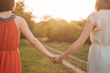 İki kız arkadaş gün batımında ormanda birlikte yürürler. Güzel bir yaz havası var. İkisi de elbise giymiş..