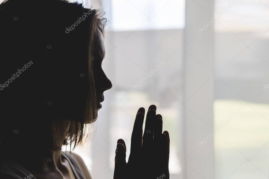 Silhouette of girl at window of clasped hand in gesture of prayer.