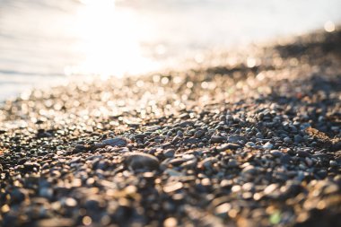 Deniz kenarında Bokeh etkisi olan küçük taşlar. Bulanık dekoratif arka plan, metin için yer. Yaz duvar kağıdı, güneşli gün batımı ışığı.
