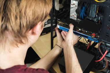 Genç adam bir bilgisayar sistemi ünitesini tamir ediyor, parçaları, video kartı ve sabit diski değiştiriyor, yeni parçalar ayarlıyor. Bilgisayar Onarım Sihirbazı.