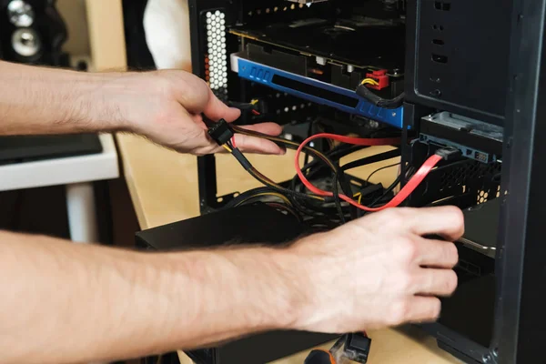 Joven repara una unidad de sistema informático, cambia partes, tarjeta de vídeo y disco duro, establece nuevos componentes. Asistente de reparación de computadoras. —  Fotos de Stock