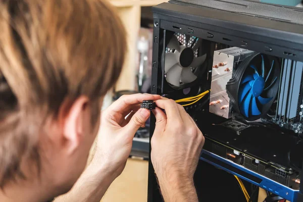 Joven repara una unidad de sistema informático, cambia partes, tarjeta de vídeo y disco duro, establece nuevos componentes. Asistente de reparación de computadoras. — Foto de Stock