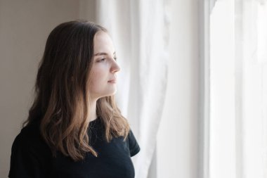 Pencerenin yanında siyah tişörtlü güzel bir kadının portresi. Üzgün, düşünceli kız düşüncelerinde kayboldu. Farkındalık kavramı.