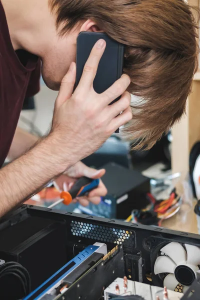 Joven repara una unidad de sistema informático, cambia partes, tarjeta de vídeo y disco duro, establece nuevos componentes. Asistente de reparación de computadoras. — Foto de Stock