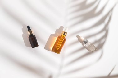 Beyaz arka planda beyaz, turuncu ve siyah serum şişeleri. Palmiye dalının gölgesi. Kozmetik modeli. Metin ve resimler eklenecek yer. Üst Manzara. Düz yatıyordu.
