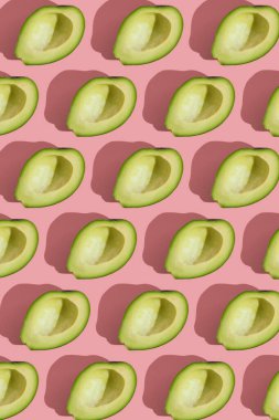 Pembe arka planda çekirdeksiz yeşil avokado modayı. Yaratıcı gıda dokusu.