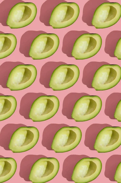 Трендовый узор в стиле полубезсеменного зеленого авокадо на розовом фоне с жестким светом. Творческая текстура продуктов питания. — стоковое фото